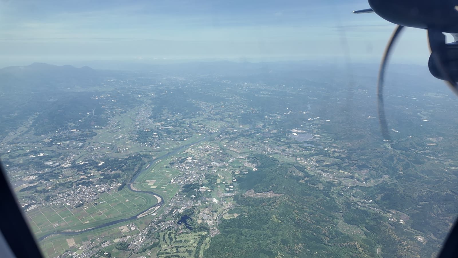 プロペラ機の窓から見た地上の街並みと川